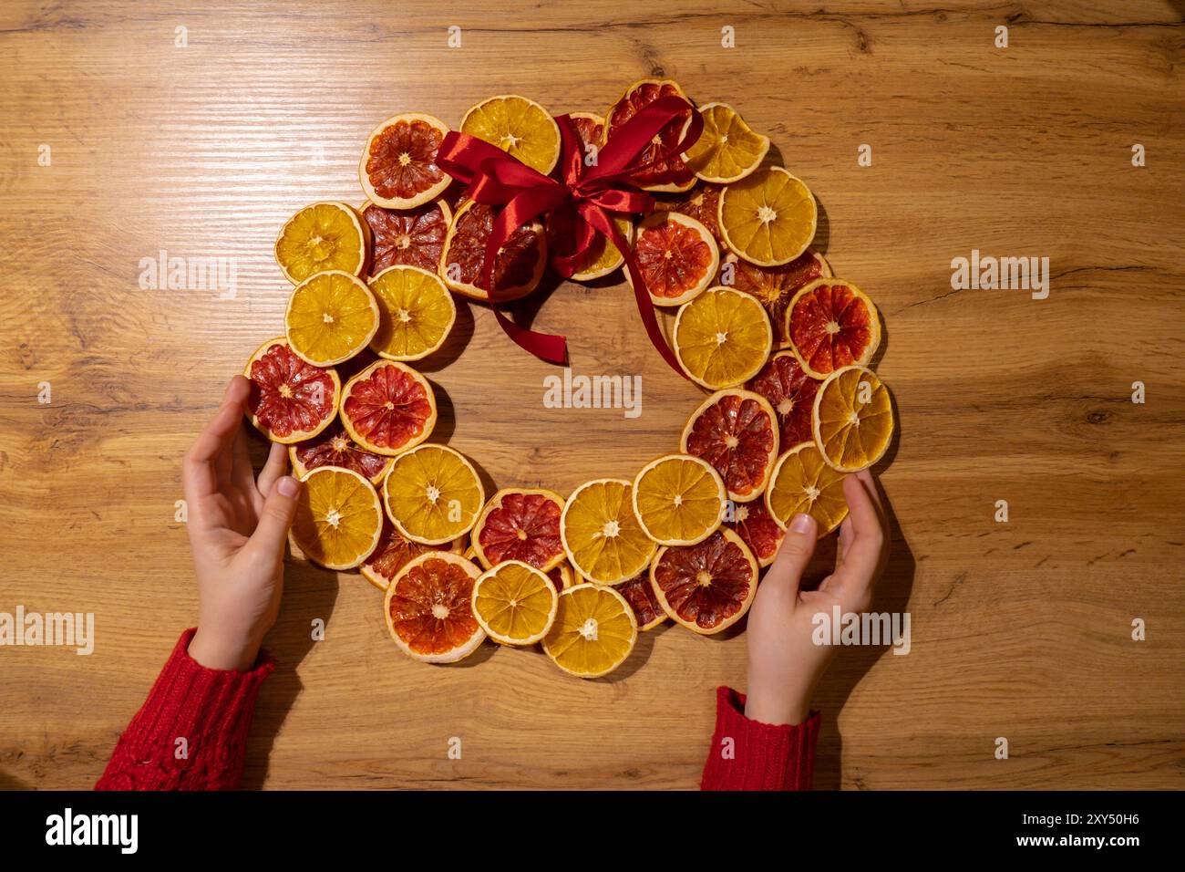 Istruzioni passo dopo passo sulla preparazione di una corona di Natale fatta a mano con frutta secca arance e pompelmo. Mani femminili che creano decorazioni artigianali fatte in casa. Festa di Capodanno. Vacanze invernali Foto Stock