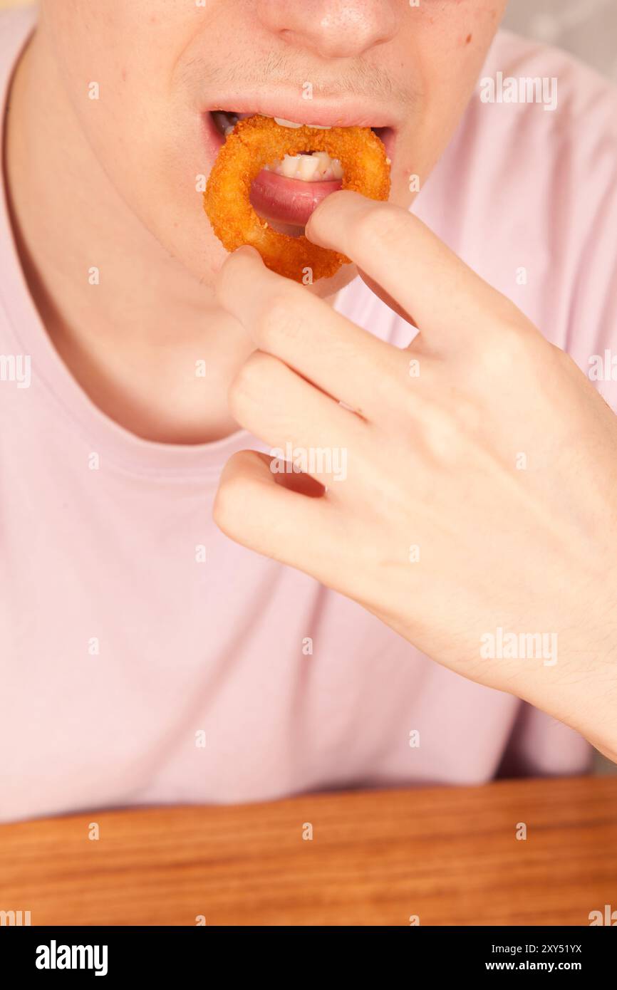 Un uomo caucasico mangia con le mani anelli di cipolla fritti freschi, cultura fast food americana Foto Stock
