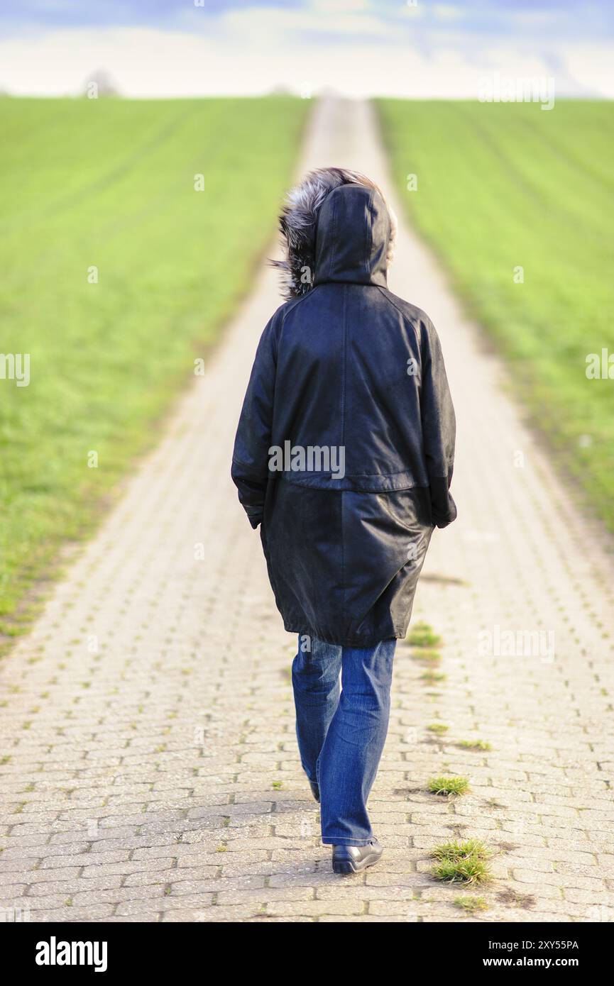 Una donna single sul retro che cammina lungo una corsia di campagna Foto Stock