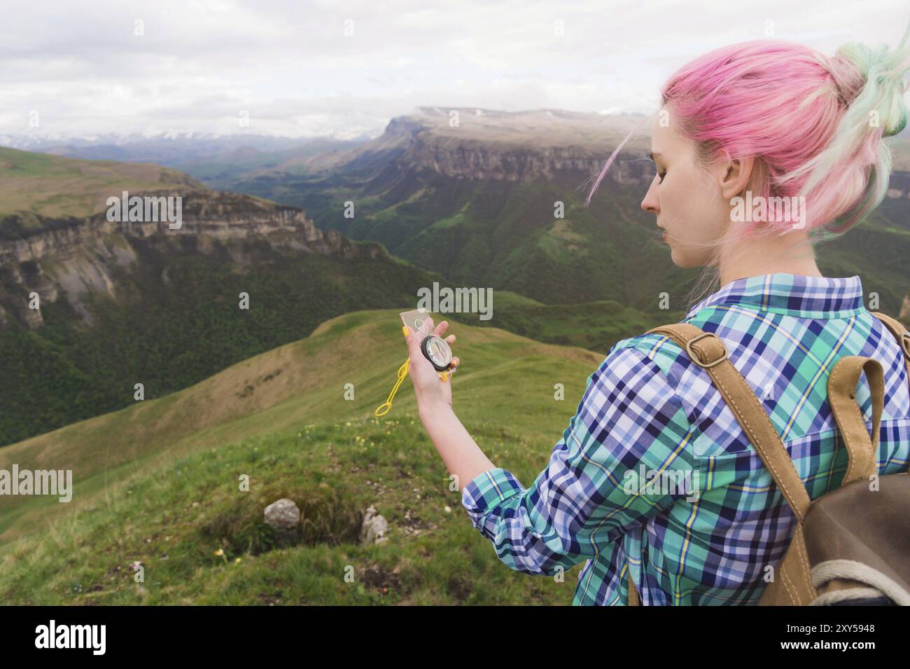 Una ragazza hipster viaggiava con un blogger in una camicia a quadri e con capelli multicolori usando una bussola sullo sfondo sullo sfondo del Caucasi Foto Stock