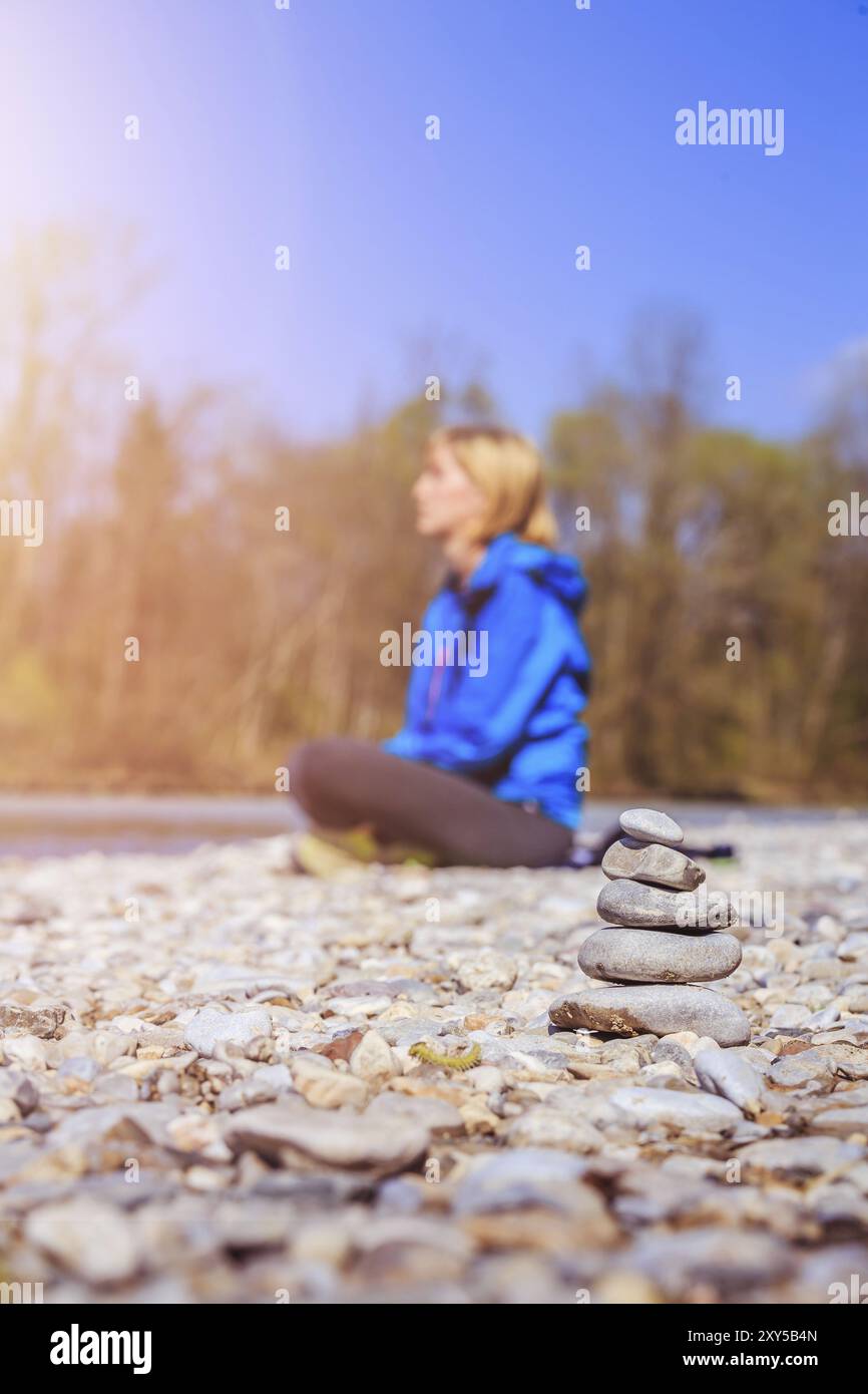 Cairn su una spiaggia di ciottoli, meditando una donna sullo sfondo. Sole mattutino Foto Stock