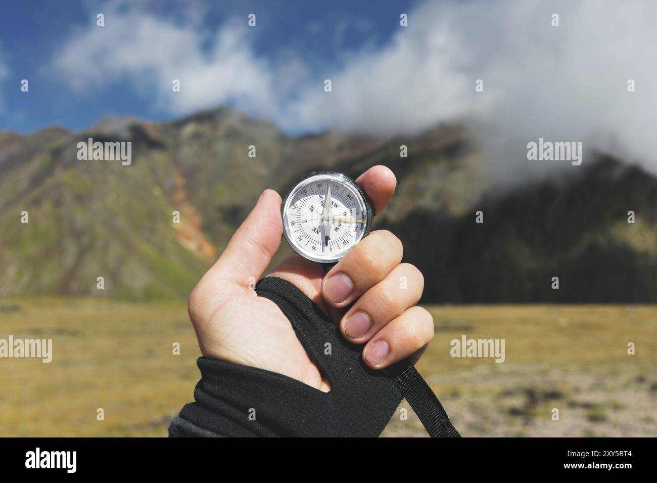 Ripresa punto di vista. Una vista in prima persona della mano di un uomo regge una bussola sullo sfondo di un paesaggio epico con scogliere colline e un cielo blu con Foto Stock