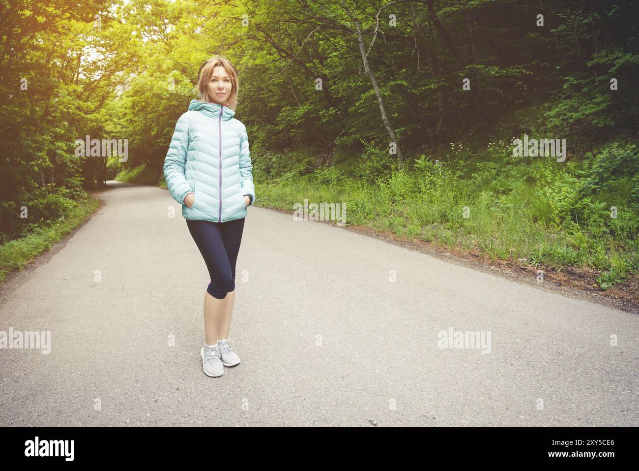 Ritratto di un'attraente bionda sportiva in una giacca leggera che indossa le cuffie bluetooth con musica o i suoni della natura mentre sono in funzione Foto Stock