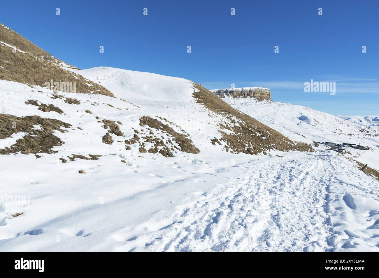 Il paesaggio di rocce caucasiche innevate sul passo Gumbashi. Altopiano innevato che passa nella montagna da tavola con un sentiero innevato in avanti Foto Stock