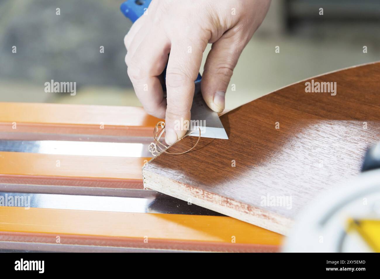 Un primo piano delle mani non ben curate del vero falegname maschile completa la finitura dei dettagli in truciolato dei mobili tagliando il bordo Foto Stock