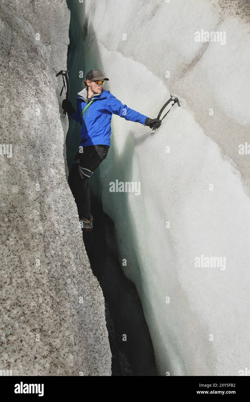 Un arrampicatore libero senza assicurazione con due assi di ghiaccio sale da una crepa nel ghiacciaio. Arrampicata libera senza corde Foto Stock