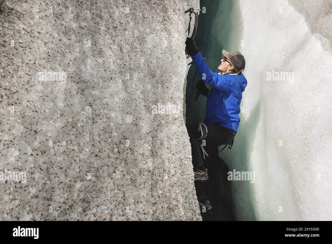 Un arrampicatore libero senza assicurazione con due assi di ghiaccio sale da una crepa nel ghiacciaio. Arrampicata libera senza corde Foto Stock