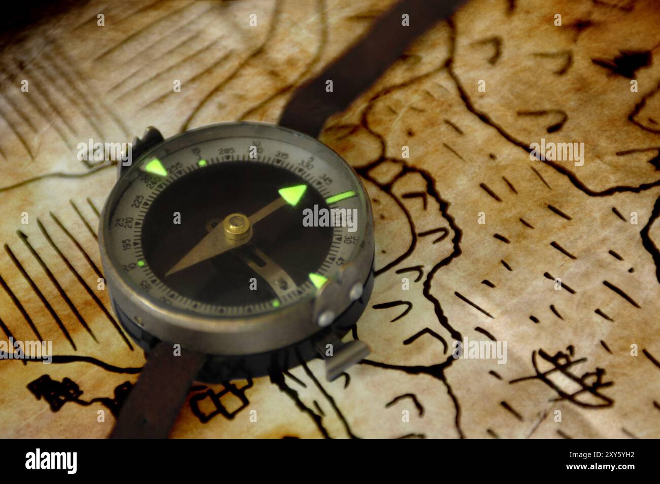Bussola magnetica vintage con puntatore verde illuminante al fosforo su una vecchia mappa Foto Stock