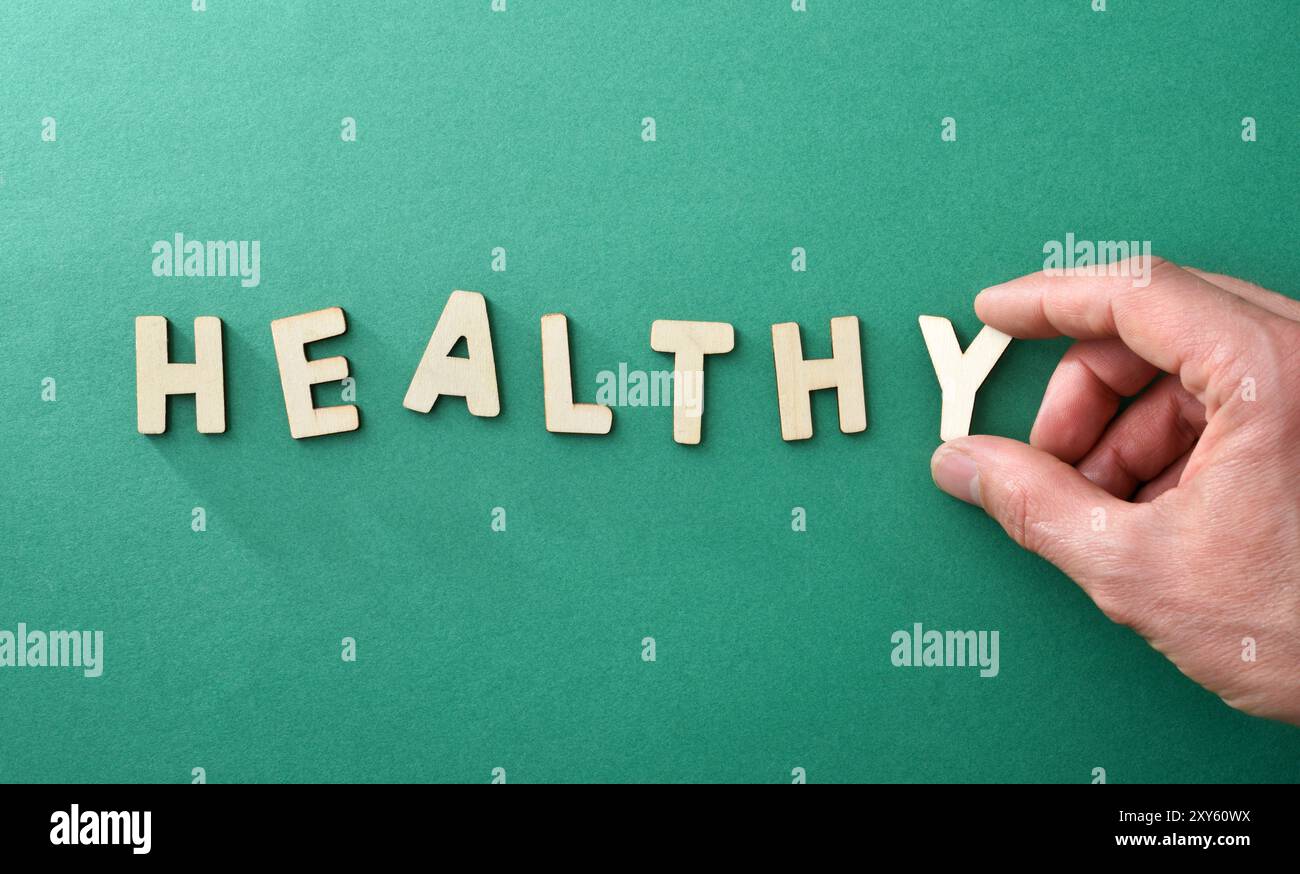Concetto di vita sana con le mani che formano la parola sana con lettere di legno su sfondo verde. Vista dall'alto. Foto Stock
