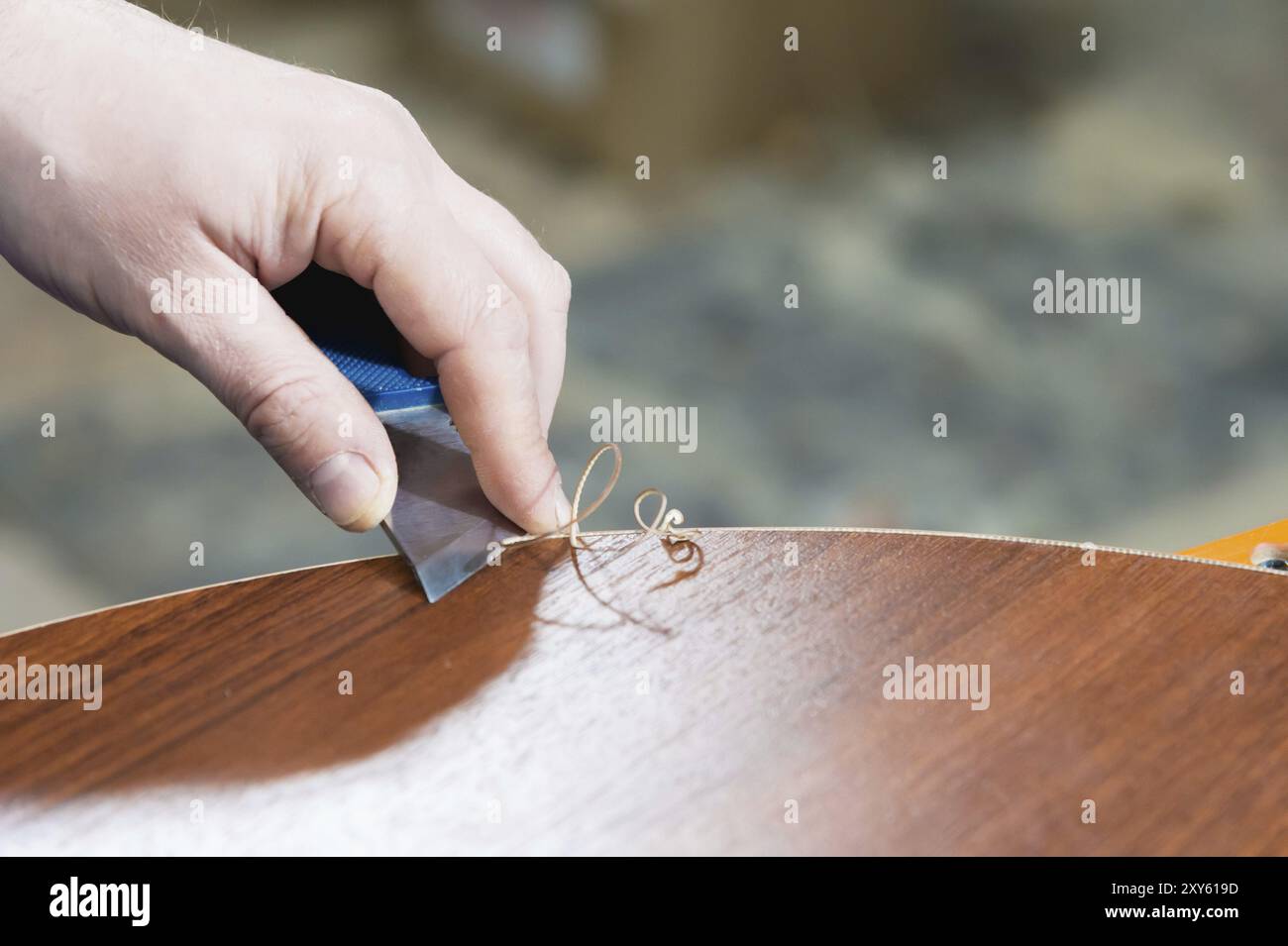 Un primo piano delle mani non ben curate del vero falegname maschile completa la finitura dei dettagli in truciolato dei mobili tagliando il bordo Foto Stock