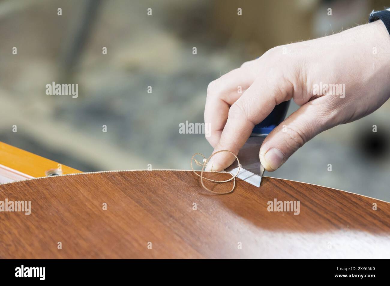 Un primo piano delle mani non ben curate del vero falegname maschile completa la finitura dei dettagli in truciolato dei mobili tagliando il bordo Foto Stock