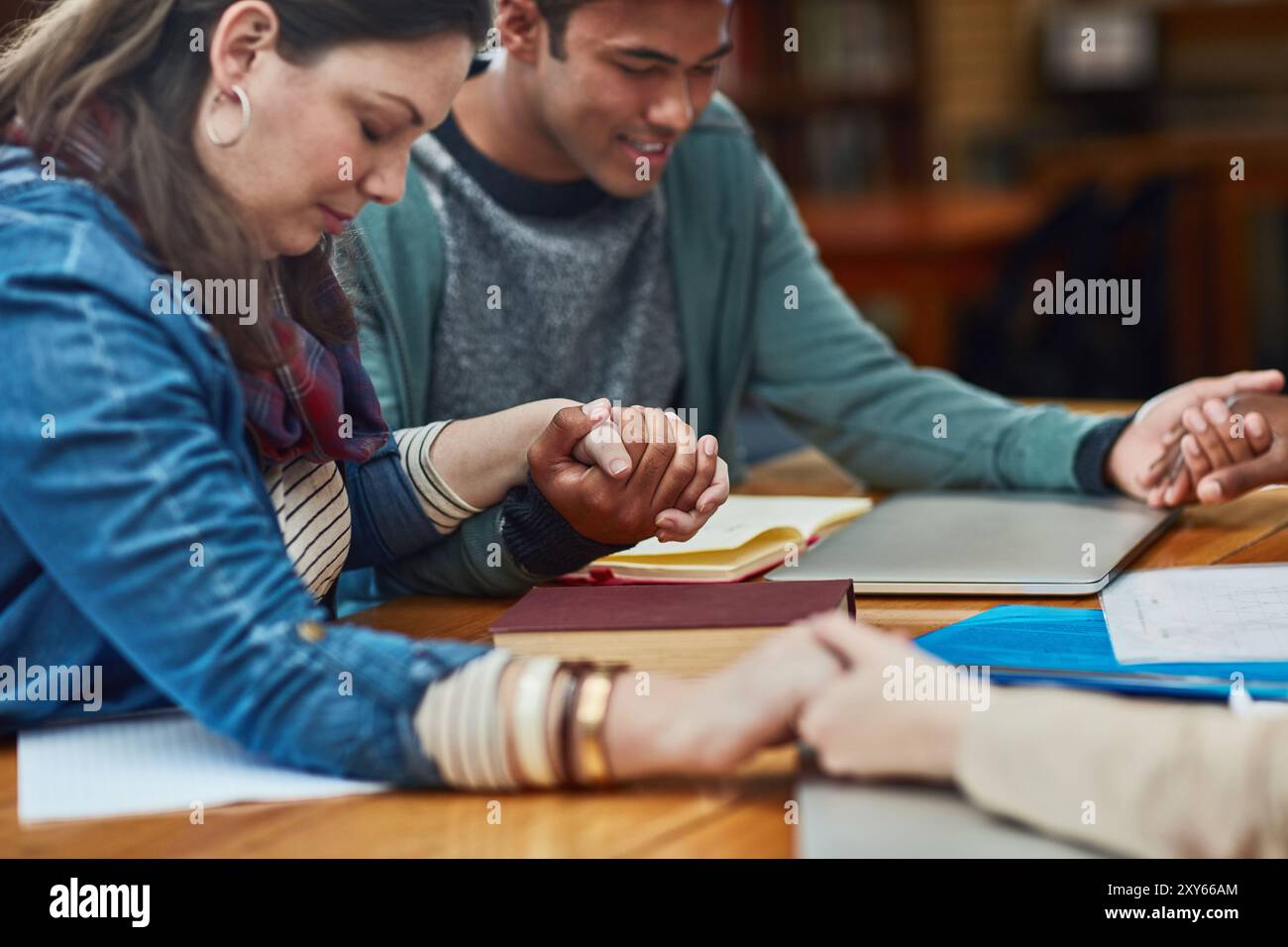 Gruppo, studio della bibbia o tenersi per mano a tavola per la preghiera, la gratitudine o il culto alla tecnologia. Persone religiose, gesto spirituale o incontro in biblioteca per Foto Stock