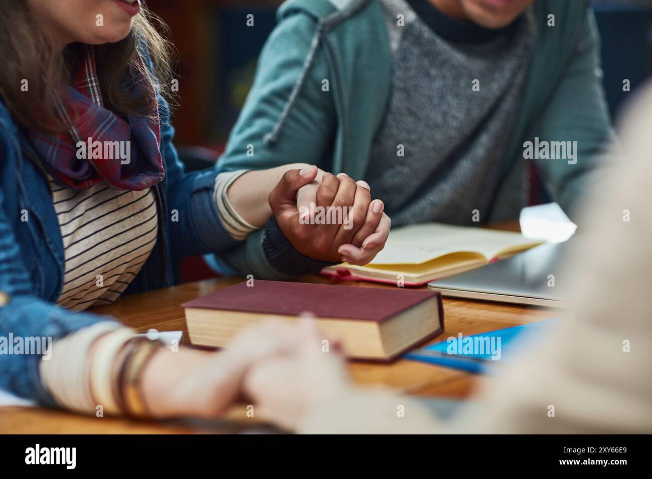 Le persone, la bibbia studiano o si tengono per mano a tavola per il culto, la gratitudine o la preghiera al libro. Gruppo religioso, gesto spirituale o incontro in biblioteca per Foto Stock
