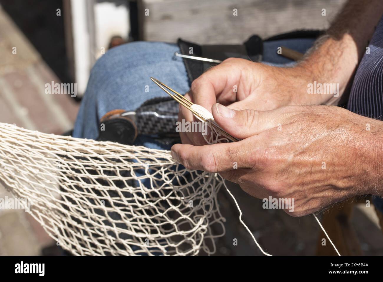 Enkhuizen, Paesi Bassi. Giugno 2022. Le mani di un pescatore che ripara reti da pesca con ago e filo. Primo piano Foto Stock