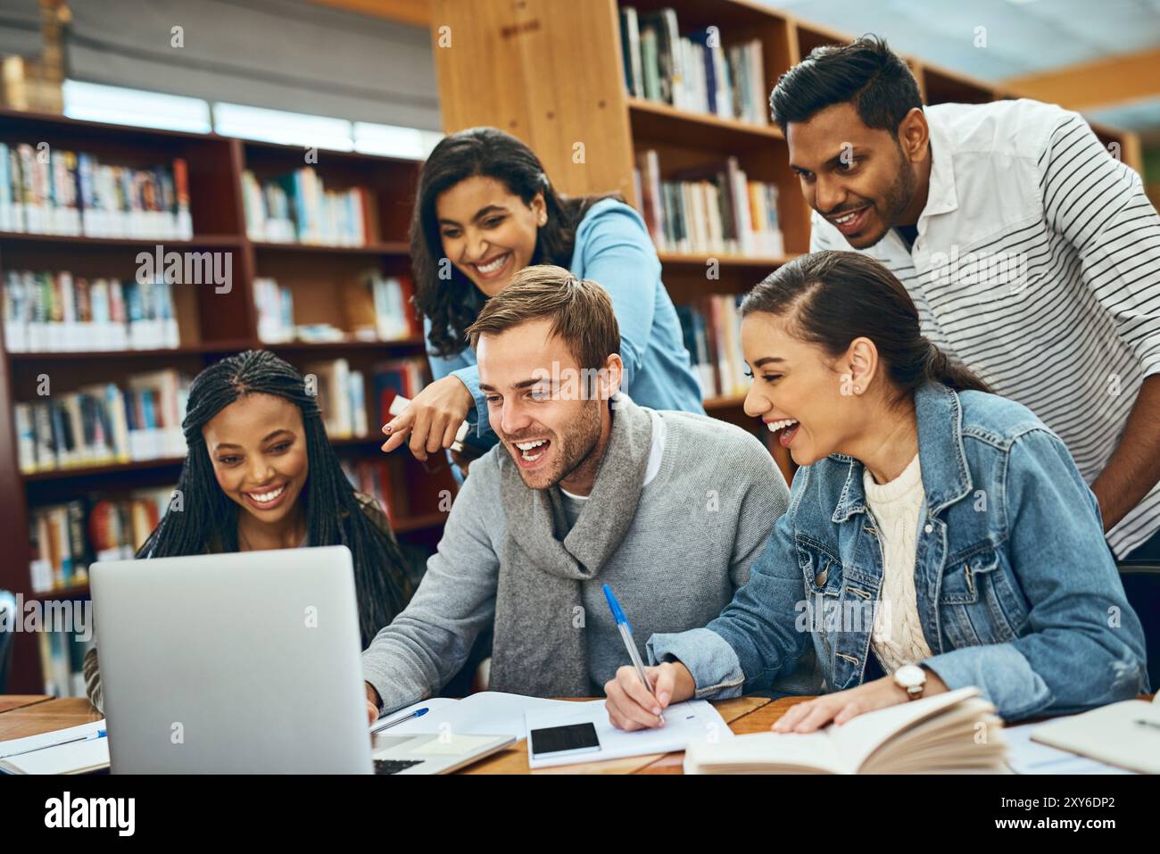 Istruzione, studenti e ridendo di un portatile in biblioteca per progetti di ricerca, meme divertenti e compiti creativi. Gruppo di studio sulla diversità, libri e. Foto Stock