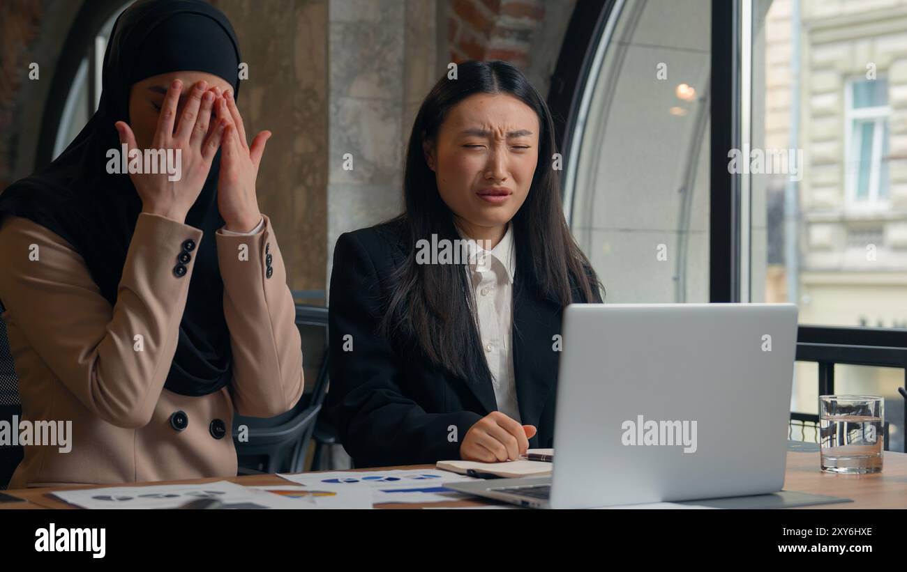 Due donne d'affari multirazziali donna asiatica coreana ragazza musulmana hijab islamico donna d'affari ufficio donne d'affari che guardano schermo portatile terribile Foto Stock