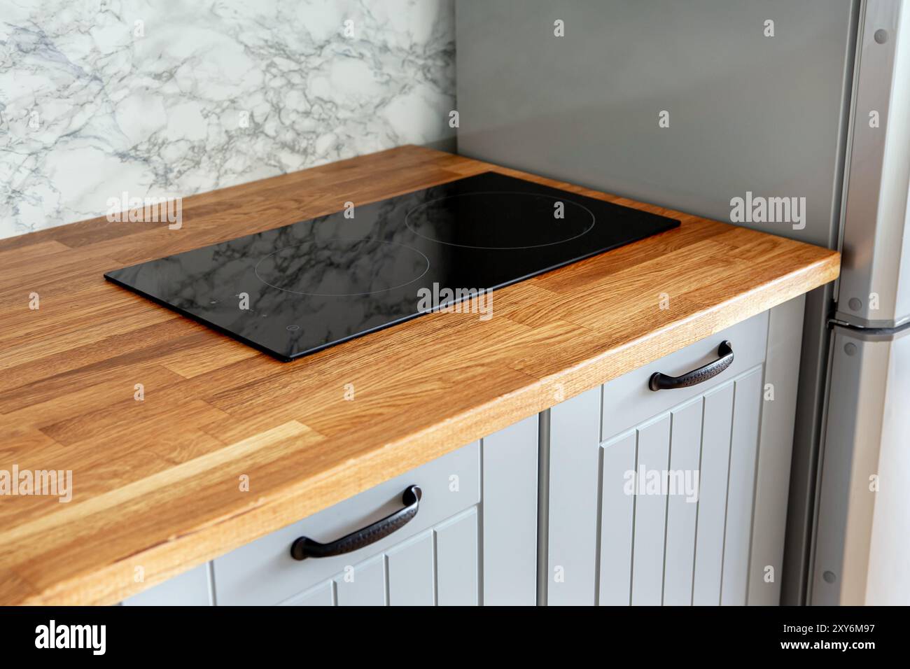 Piano di appoggio in legno naturale con piano cottura elettrico incorporato. Piccola cucina minimalista con armadietti grigi. Foto Stock