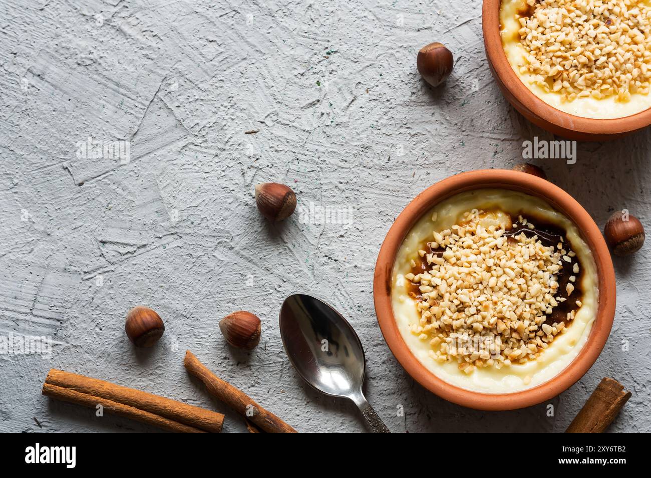Budino di riso al forno sutlac per dessert lattiginoso turco in casseruola con bastoncini di cannella e nocciole tritate Foto Stock