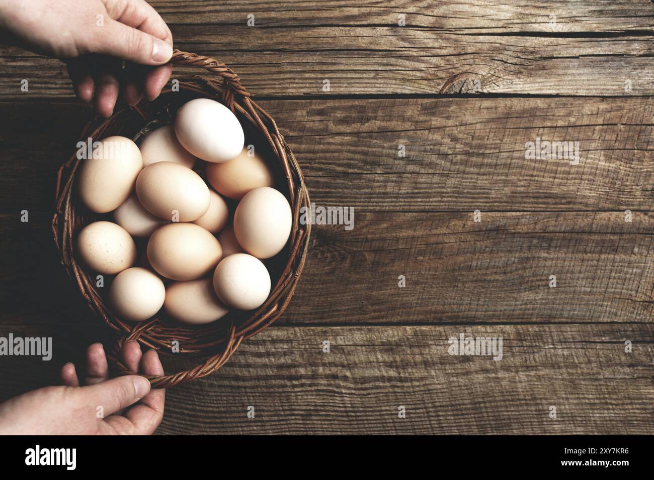 Piatto con le mani che reggono cesto con uova di pollo biologiche su sfondo di legno. Concetto domestico biologico con uova di free-range e pascolo rai Foto Stock