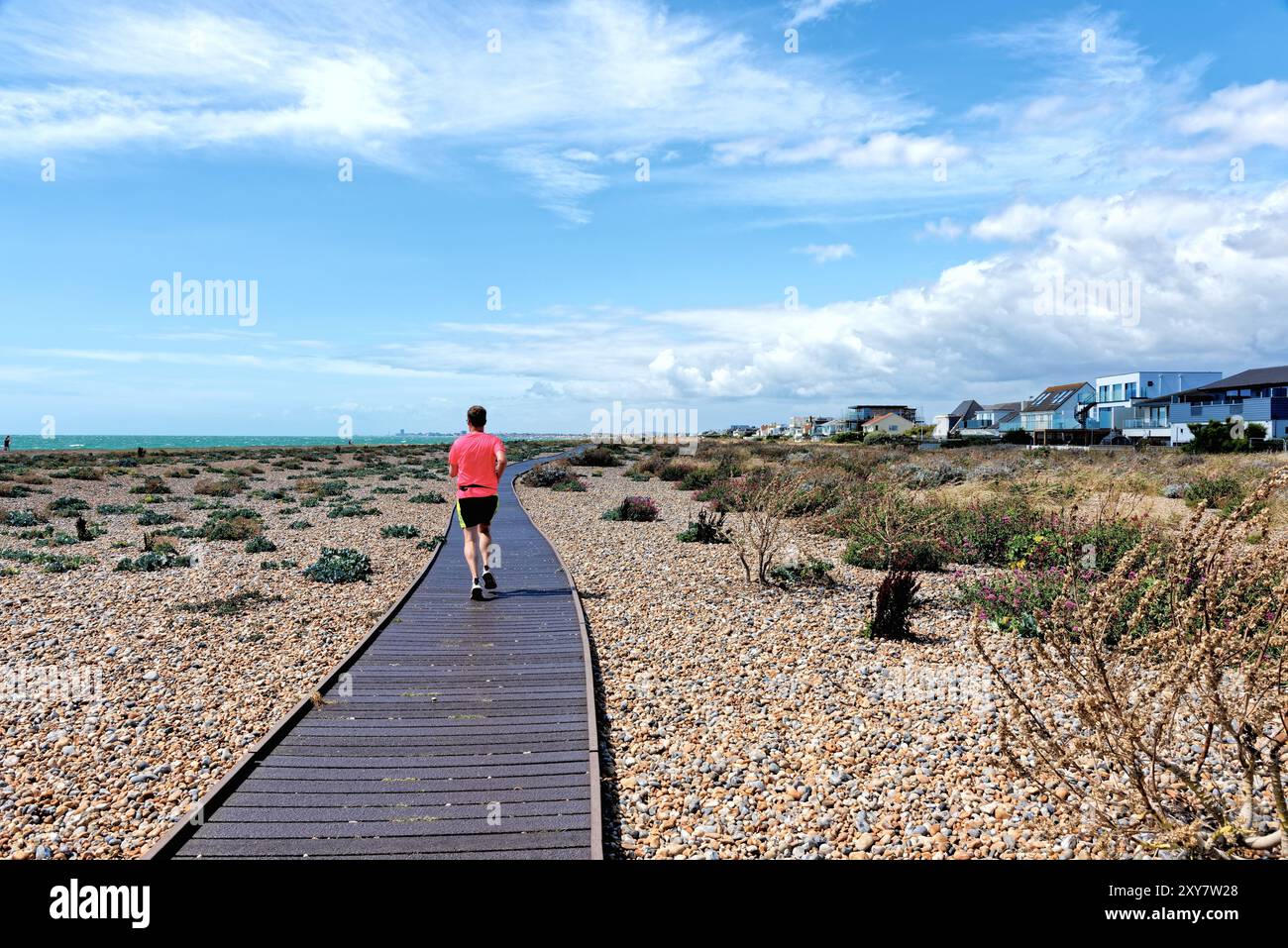 Un giovane corridore maschile in maglietta rossa sul lungomare di Shoreham Beach in una calda giornata estiva a ovest del Sussex Inghilterra regno unito Foto Stock