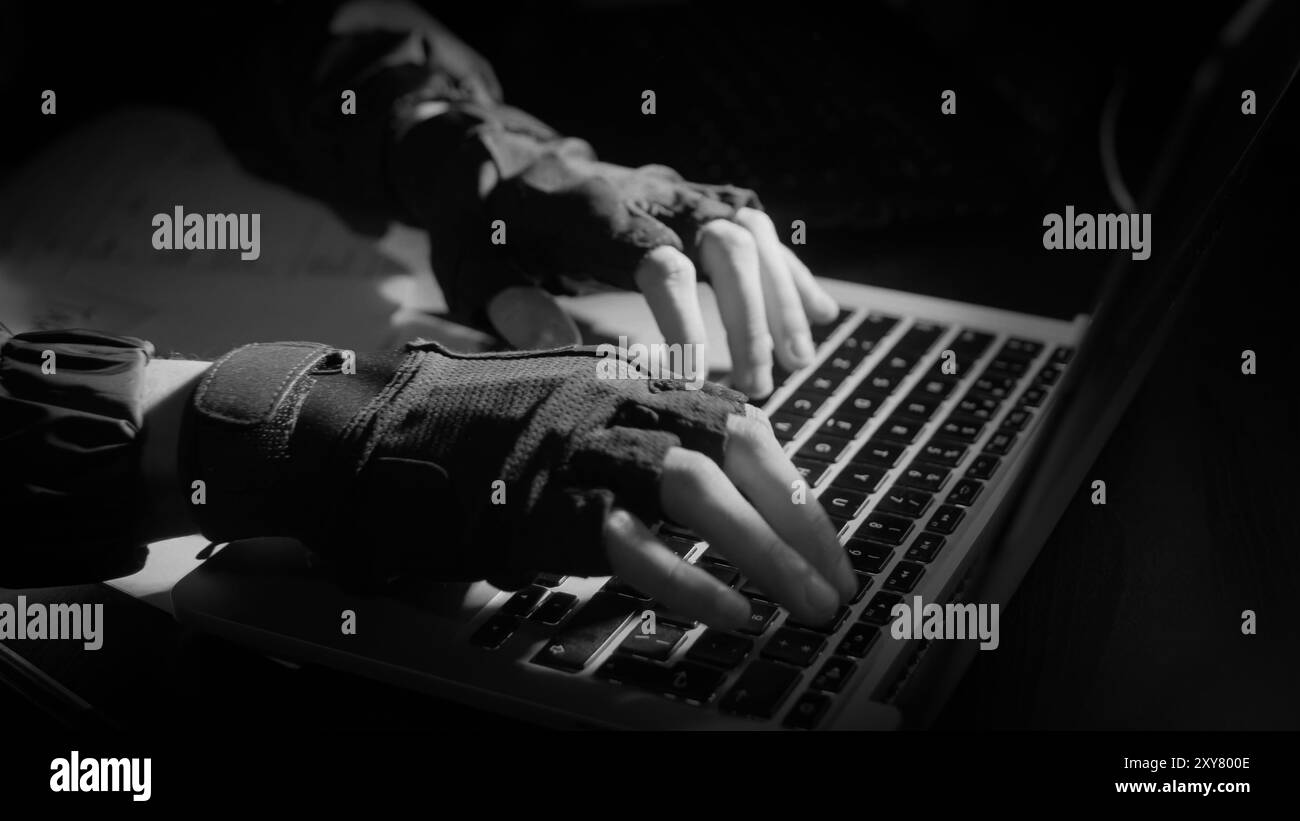 Foto ritagliata di un giovane uomo che scrive a mano su un computer portatile mentre lavora in una stanza d'ufficio nera. hacker hacking del server al buio Foto Stock