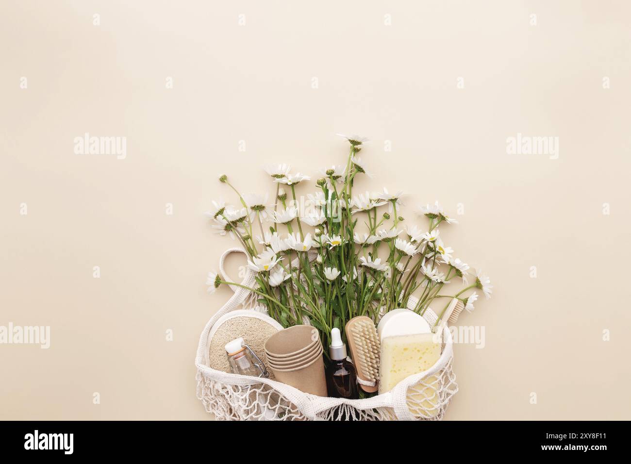 Eco friendly concetto estivo su sfondo beige con borsa eco shopping, fiori camomilla bianchi, accessori bagno, spazzole, bottiglia di olio essenziale, sapone Foto Stock