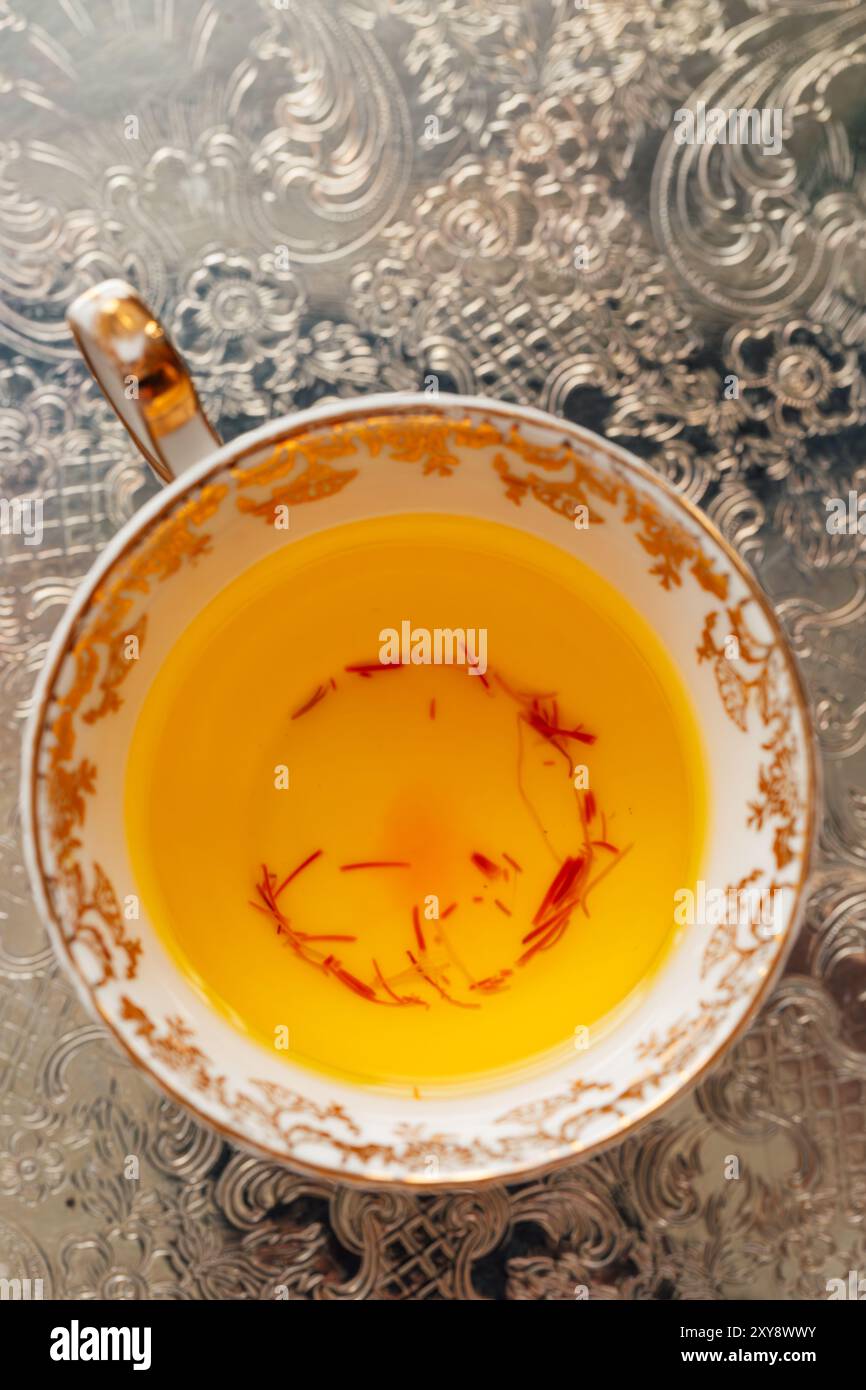 vista ad angolo alto del tè allo zafferano giallo con fili rossi in un vassoio d'argento decorato oro e bianco Foto Stock