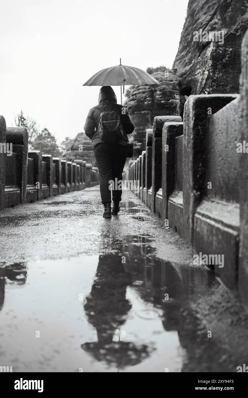 Una figura solitaria con un ombrello che cammina su uno storico ponte di pietra dopo la pioggia. Foto in bianco e nero con riflessi nelle pozzanghere Foto Stock