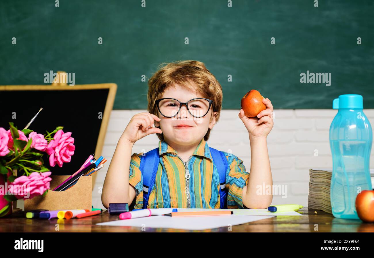 Colazione scolastica o pranzo per la salute dei bambini. Piccolo scolaro alla scrivania che mangia mele. Cibo gustoso per gli alunni. Un ragazzo carino mangia mele durante la pausa pranzo Foto Stock