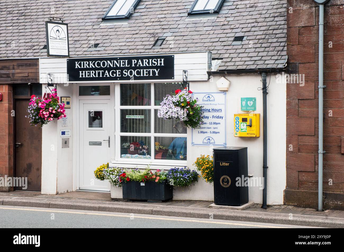 Cesti sospesi vasca di fiori e defibrillatore all'esterno dell'edificio bianco della Kirkconnel Parish Heritage Society sulla strada che attraversa Kirkconnel Scozia Foto Stock