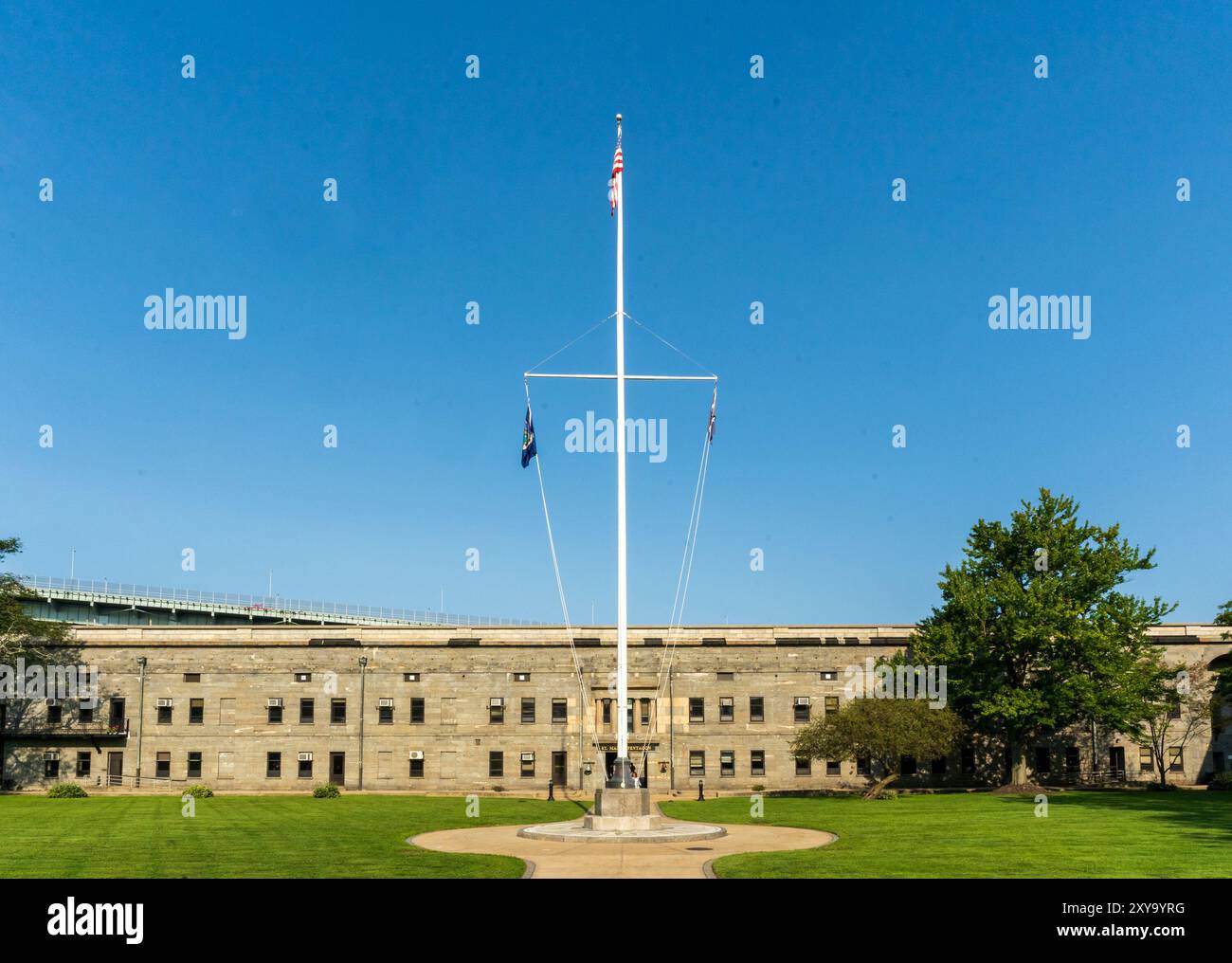 Bronx, New York - US - 24 agosto 2024 il cortile di Fort Schuyler presenta un alto albero di bandiera che sventola con orgoglio la bandiera degli Stati Uniti, posto contro la storica S del forte Foto Stock