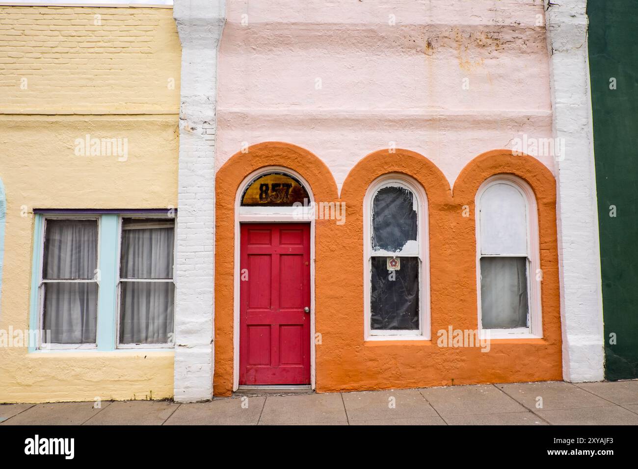 Una porta rossa unica e una facciata arancione su una strada commerciale principale Foto Stock