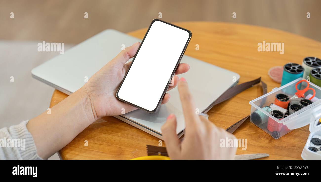 Persona che utilizza smartphone con forniture per cucire. Tecnologia e integrazione artigianale Foto Stock