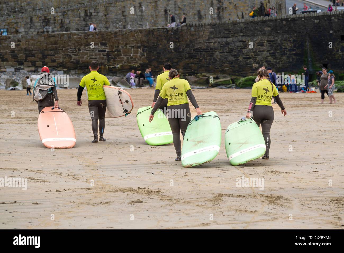 I principianti della Escape Surf School imparano a restituire le loro tavole da surf dopo aver finito una lezione con il loro insegnante di surf sulla spiaggia di Towan a Newqua Foto Stock