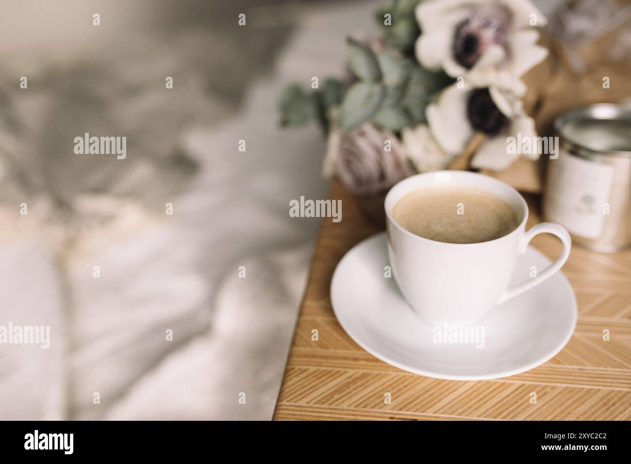 Mattina romantica. Tavolino in legno con fiori sul letto con plaid, tazza da caffè, fiori e candele. Lilla rose con eucalipto e anemoni. Inter Foto Stock