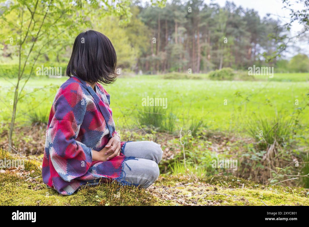 Giovanissimo colombiano donna seduta nel bosco in prossimità di pascolo verde Foto Stock