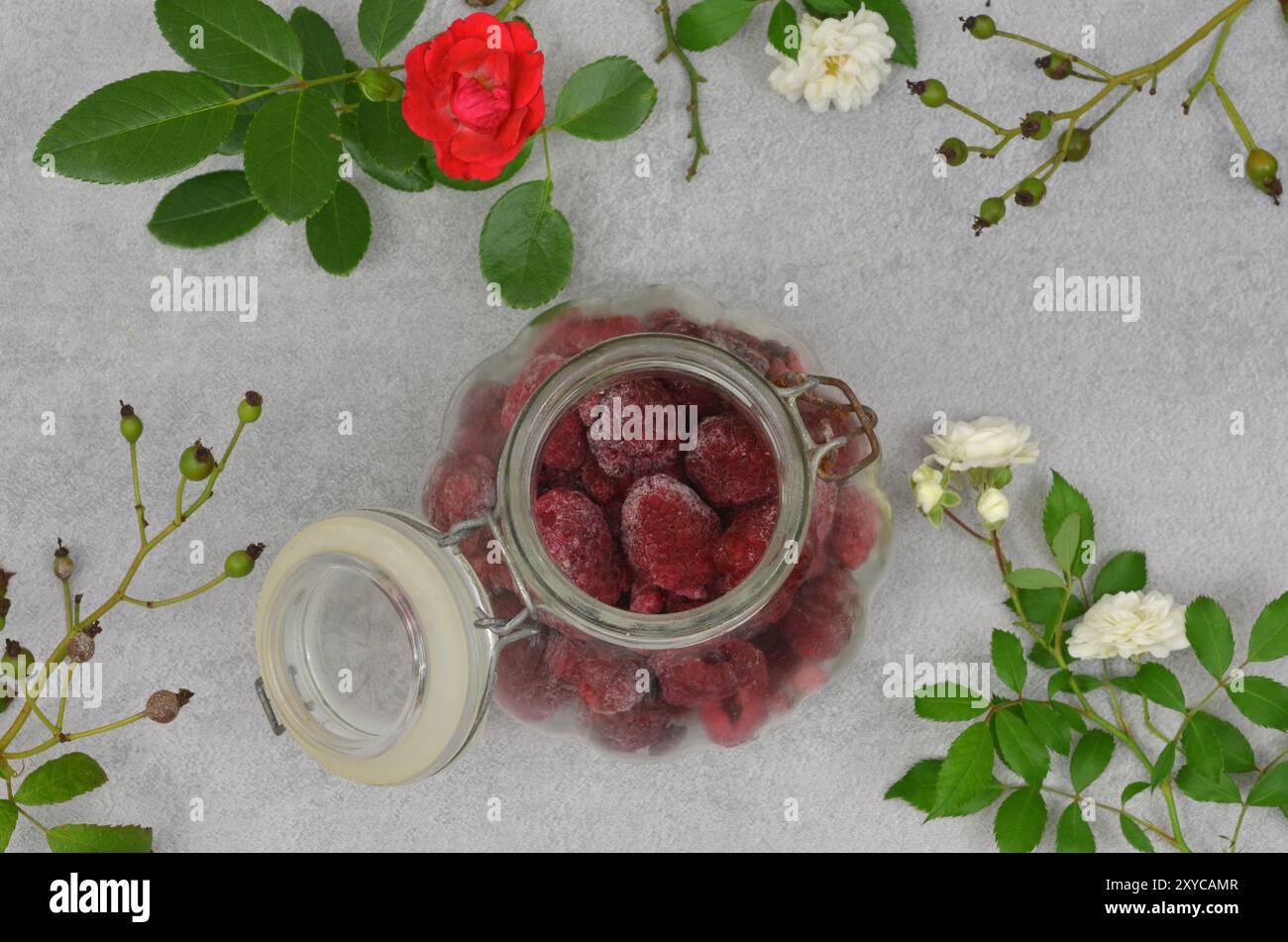 Lamponi congelati in un vaso decorato con rose e ramoscelli bianchi e rossi. Vista dall'alto. Foto Stock