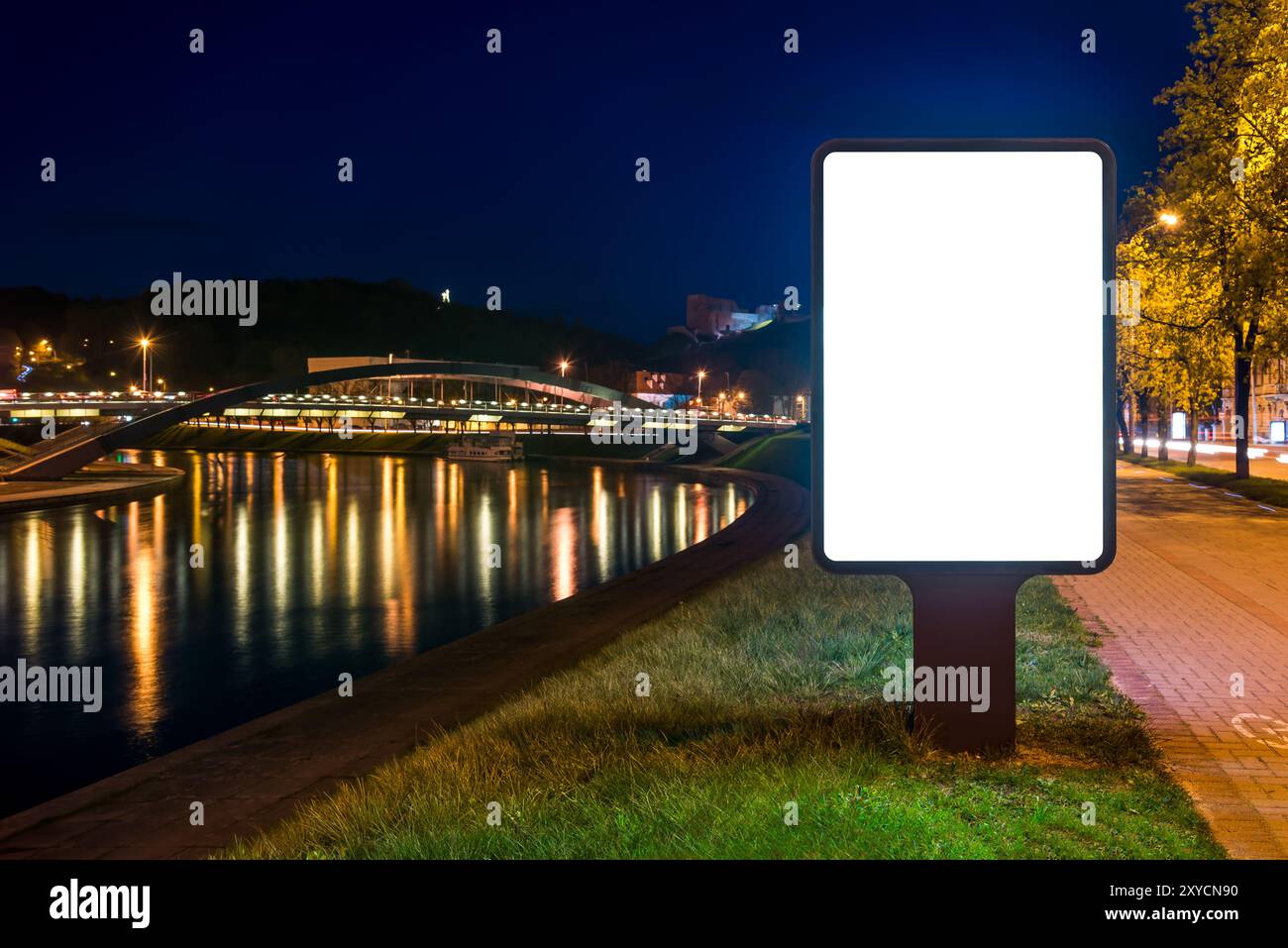Mockup di Billboard verticale sulla riva del fiume di notte. Esposizione pubblicitaria di fronte alle riflessioni della città Foto Stock