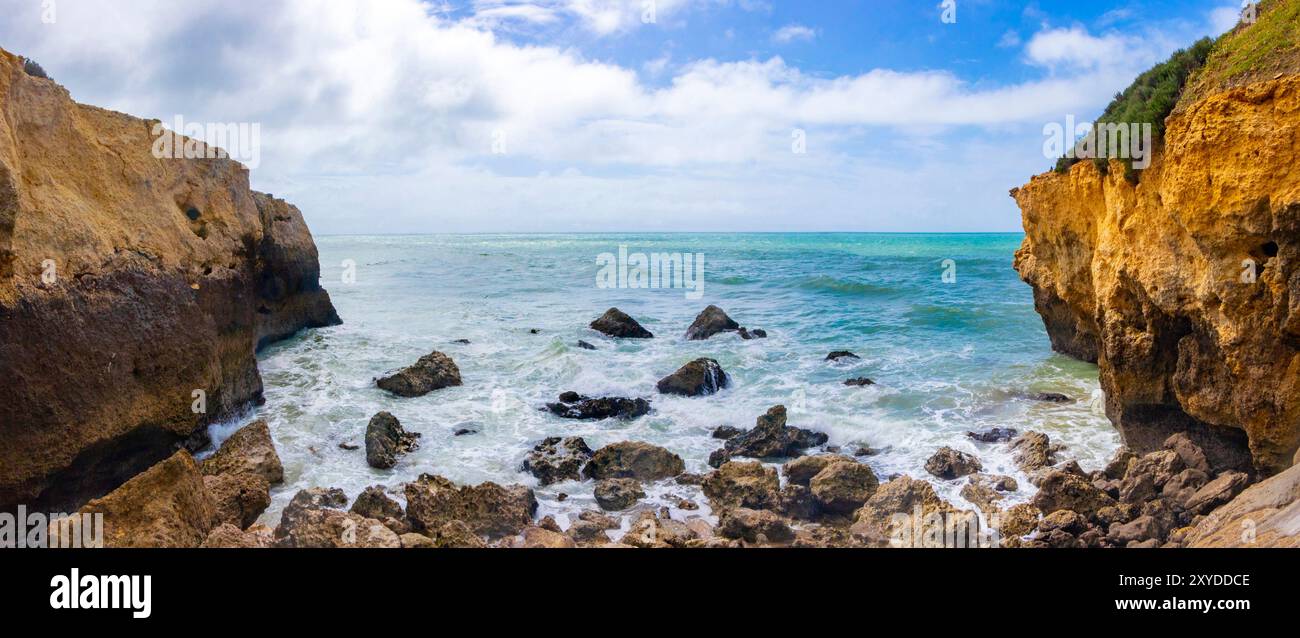 Vista panoramica di una splendida insenatura rocciosa e della costa con onde che si infrangono contro le scogliere sotto un cielo azzurro soleggiato con nuvole sparse. portogallo Foto Stock