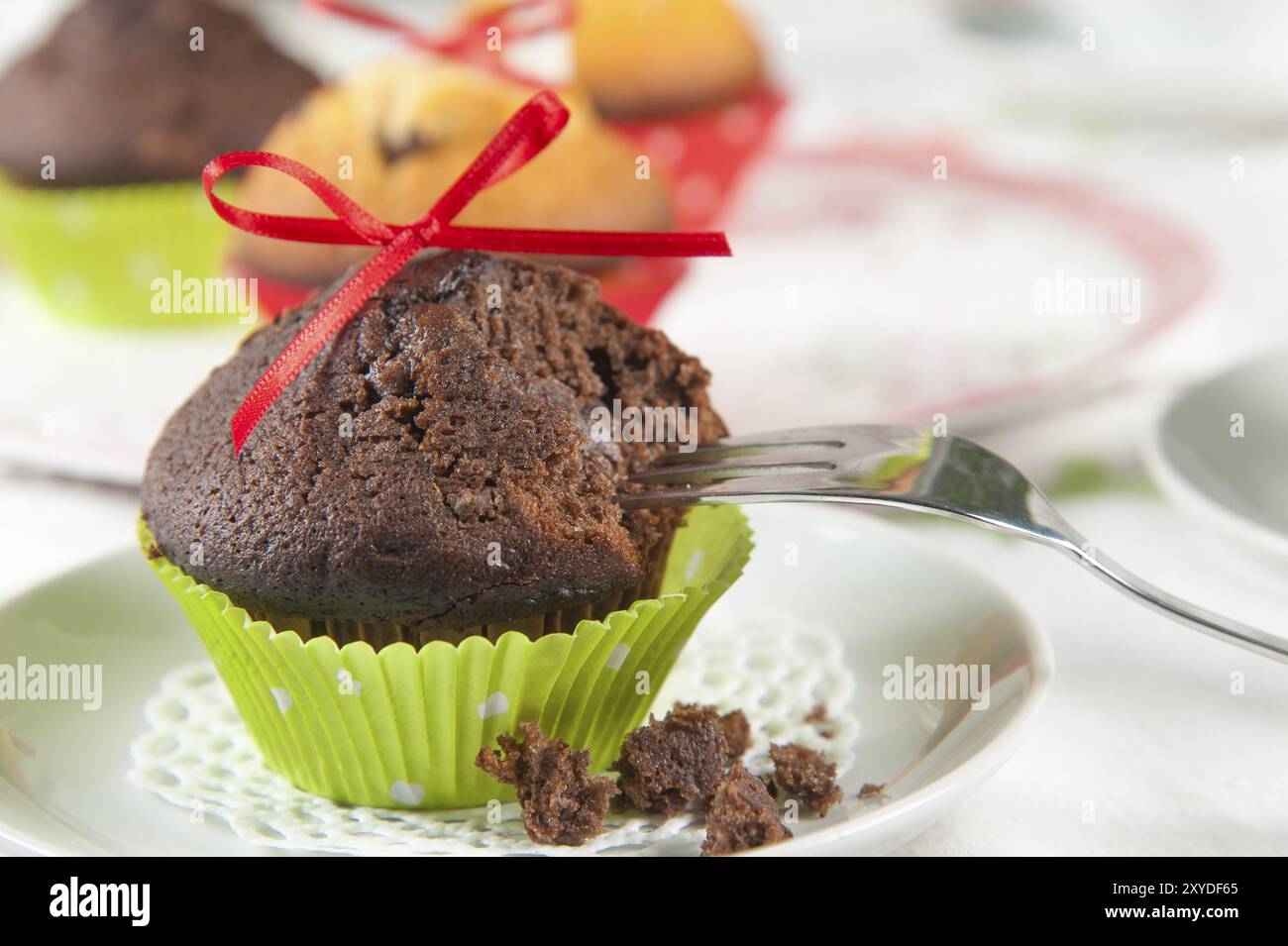 Muffin decorati con cura su un tavolino da caffè. In primo piano, un muffin al cioccolato con fiocco rosso e manica verde che è già stato assaggiato. Una CA Foto Stock