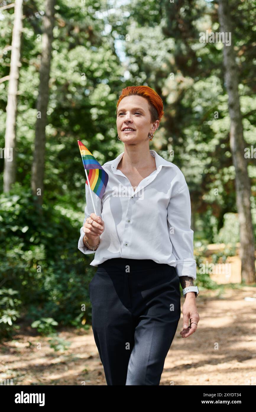 Un insegnante con una camicia bianca e pantaloni neri cammina attraverso un campus alberato, tenendo in mano una bandiera arcobaleno. Foto Stock