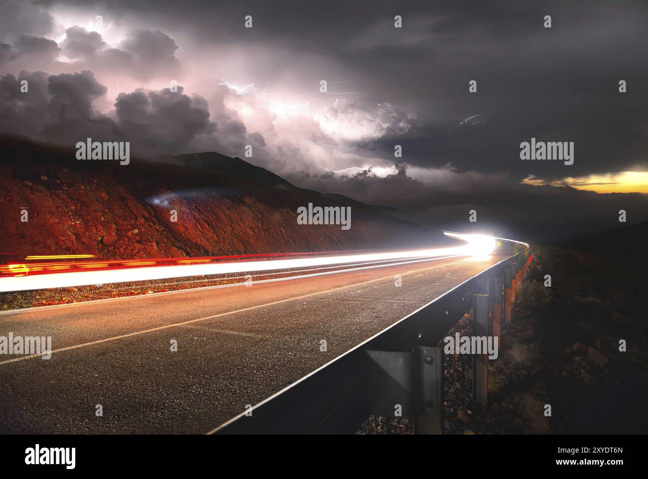 Una strada asfaltata di montagna con un'auto di passaggio al tramonto a destra e un temporale con fulmini da sinistra viene scattata con una lunga esposizione Foto Stock