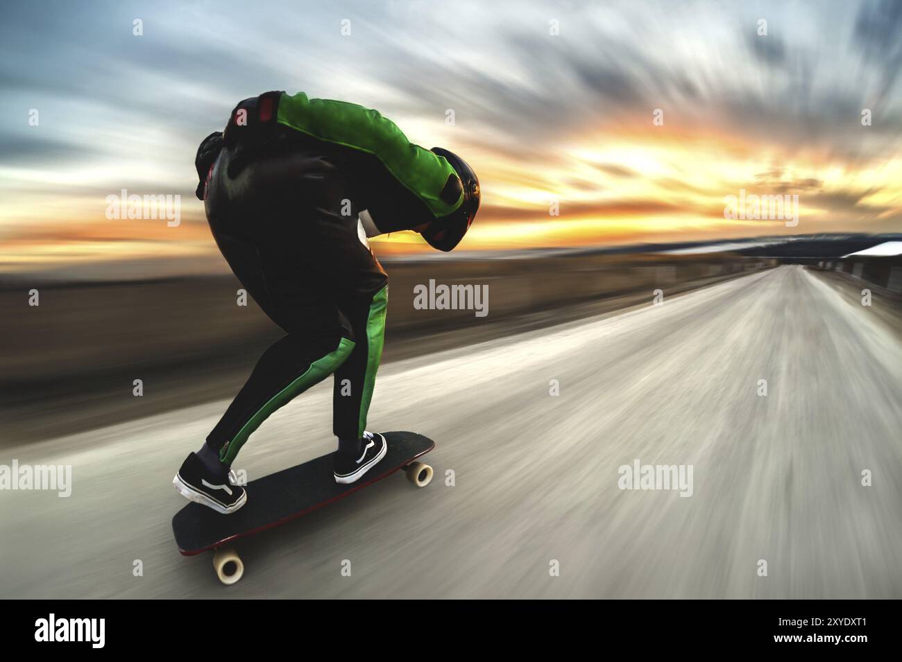 Un uomo con casco e tuta in pelle, in una speciale cremagliera ad alta velocità, cavalca su una lunga longboard per scendere in discesa a galla sullo sfondo di un beauti Foto Stock Un uomo con casco e tuta in pelle, in una speciale cremagliera ad alta velocità, cavalca su una lunga longboard per scendere in discesa a galla sullo sfondo di un beauti Foto Stock