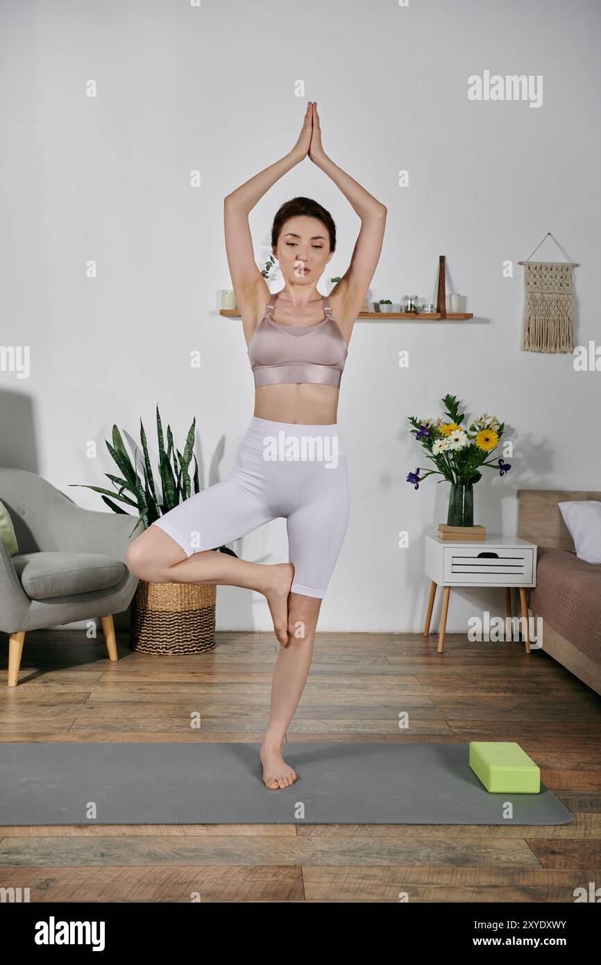 Una donna asiatica in cima a un raccolto fa yoga in posa di alberi, occhi chiusi, meditando sul suo respiro Foto Stock