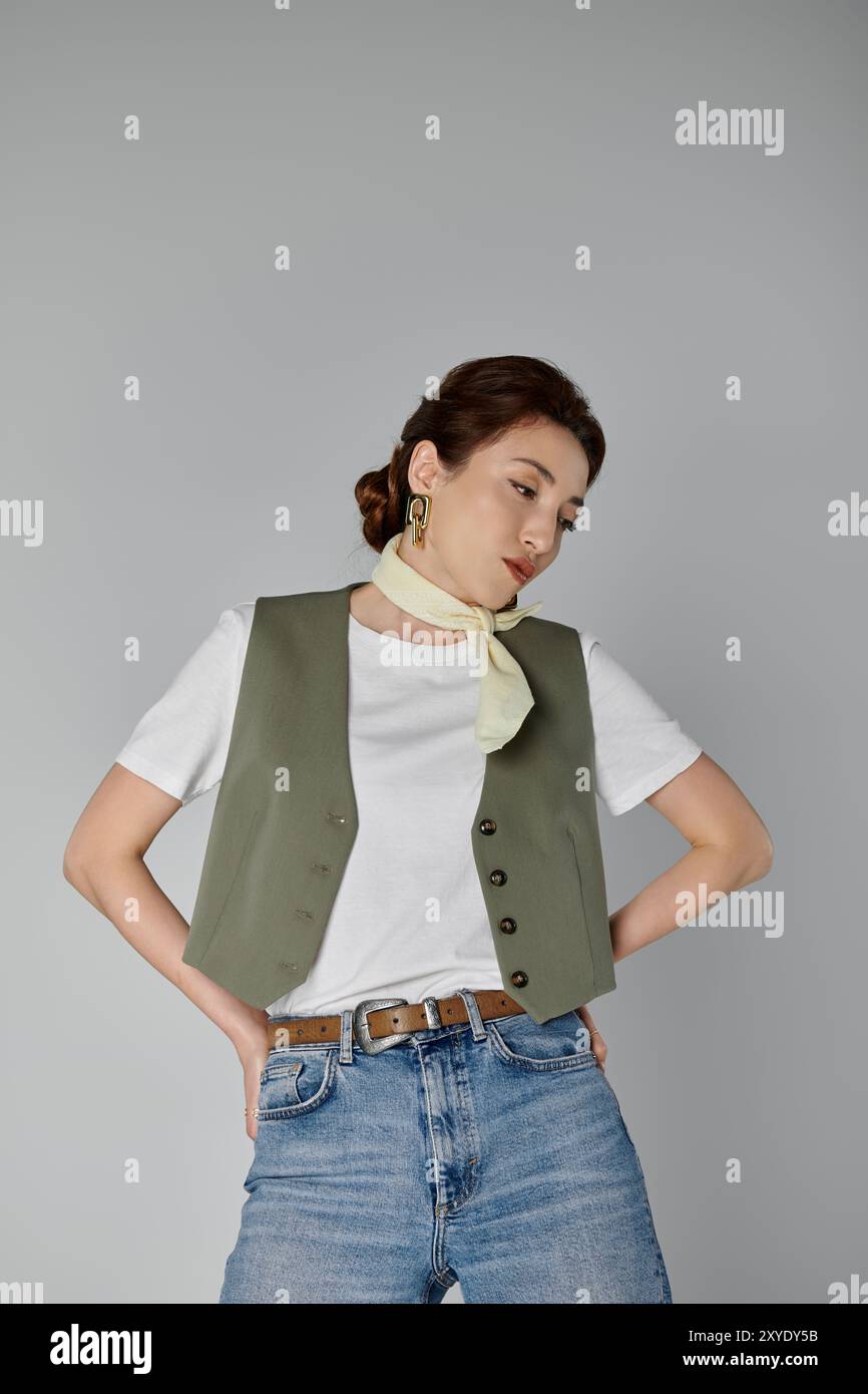 Un'elegante donna asiatica con un gilet verde e una sciarpa giallo pallido si posa su uno sfondo grigio, i suoi capelli tirati indietro in un panino. Foto Stock