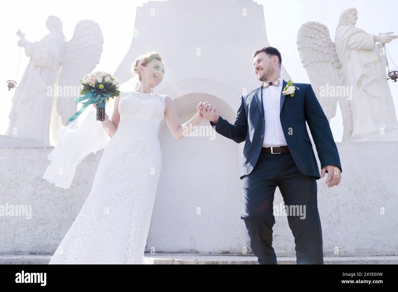 Ritratto di una bella coppia in luna di miele in un giorno di nozze con un bouquet in mano sullo sfondo di un monumento cristiano ortodosso con angeli. Foto Stock