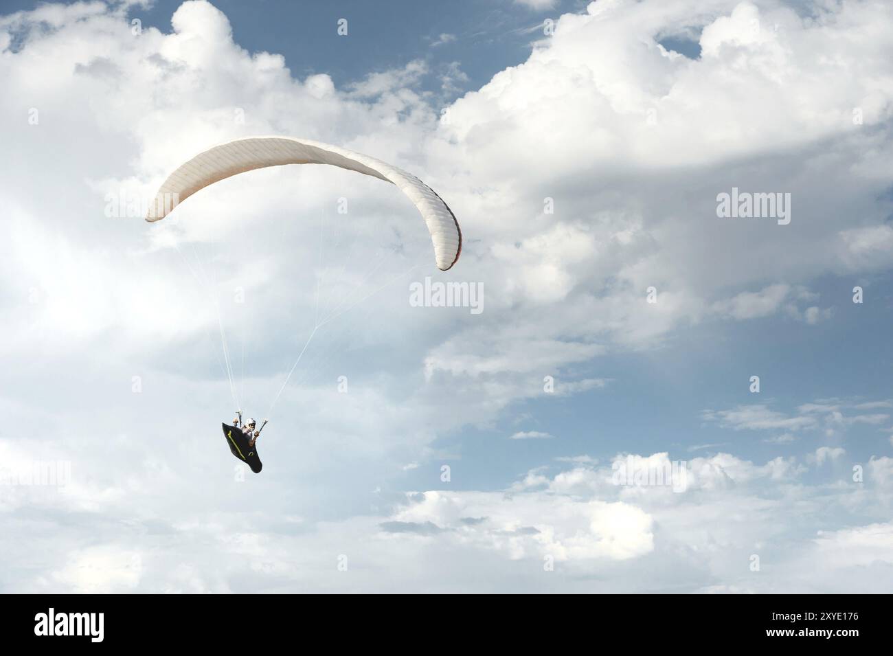 Il parapendio professionista vola su un parapendio bianco contro il cielo blu e le nuvole bianche. Sport di parapendio Foto Stock