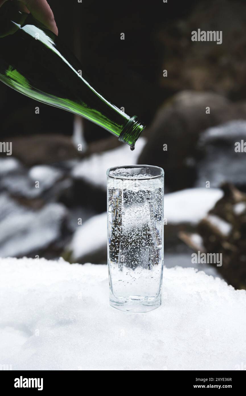 L'acqua minerale pura viene versata da una bottiglia verde di vetro in un bicchiere di vetro trasparente fino all'ultima goccia. Guardare la caduta nella bottiglia il vetro sta in piedi Foto Stock