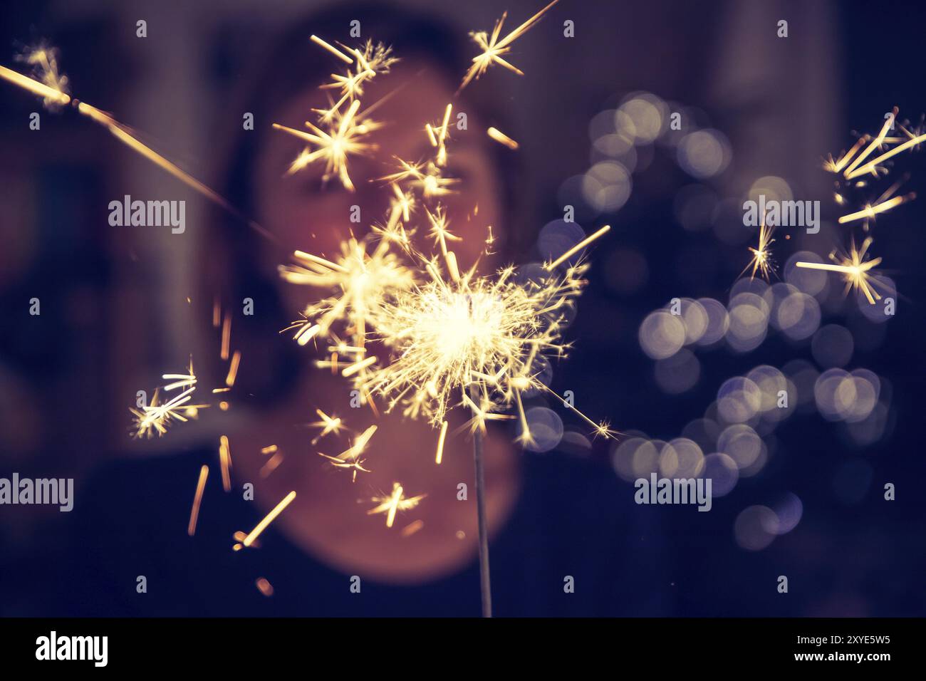 Sorridente ragazza sta tenendo un sparkler nella sua mano, indoor, luci in background Foto Stock