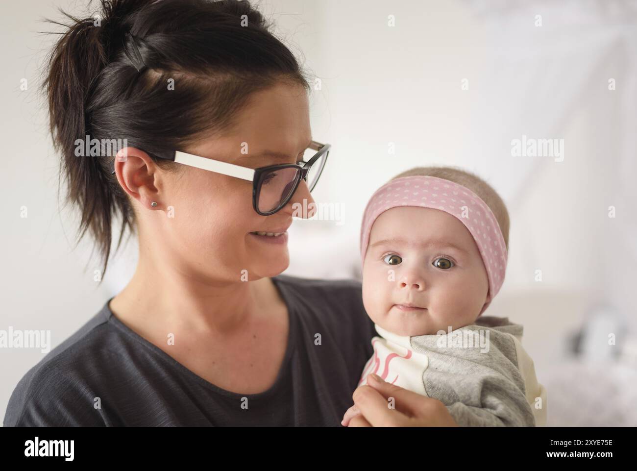 Madre che tiene bella ragazza del bambino in stanza soleggiata luminosa. Sfondo della maternità Foto Stock